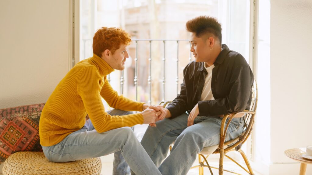 Two LGBTQIA+ individuals having a serious conversation while holding hands, representing the work of healing and repairing queer friendships