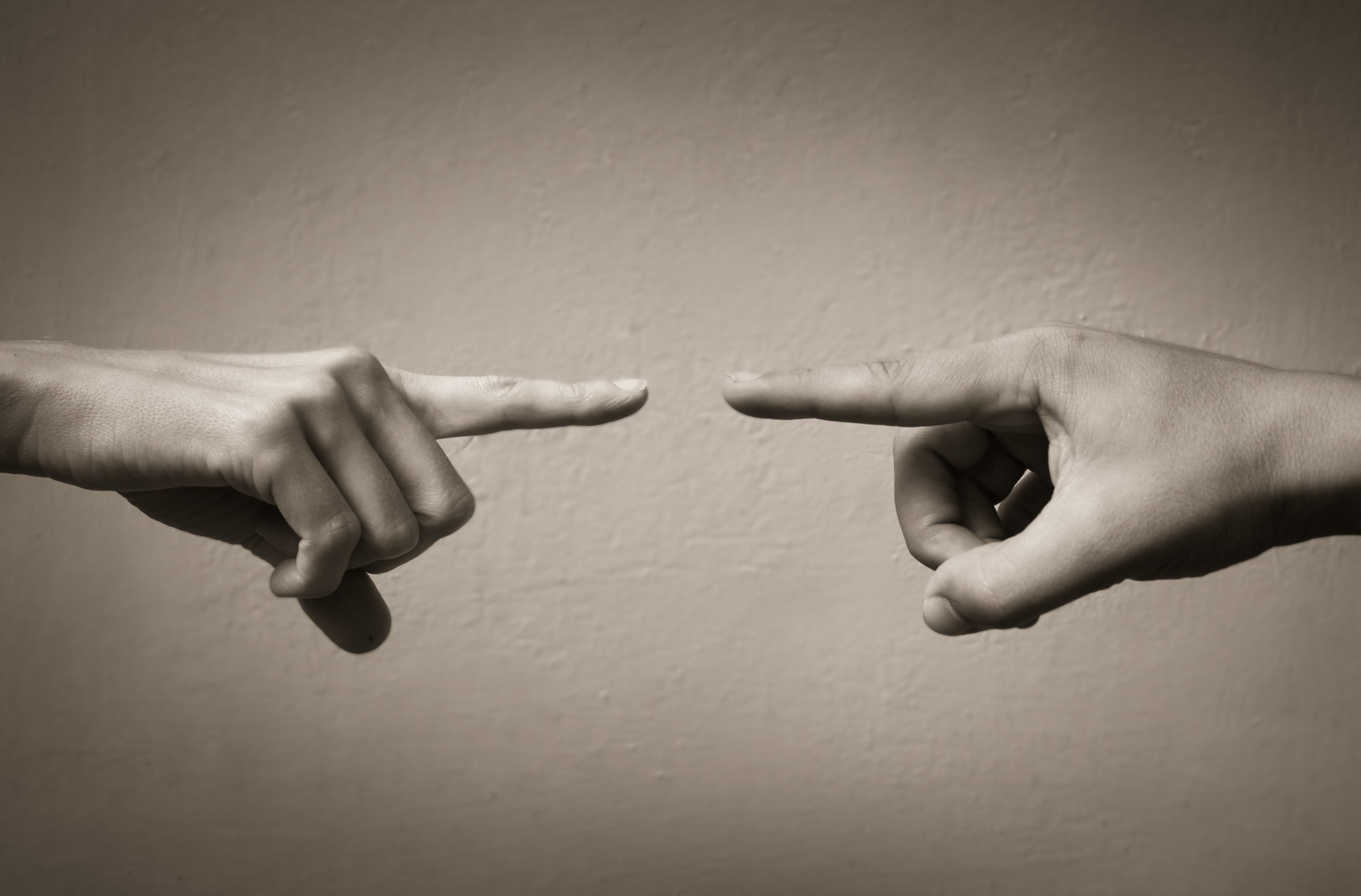 Two hands reaching toward one another with extended index fingers, separated by a small gap, symbolizing disconnection, conflict, and the challenge of human connection.