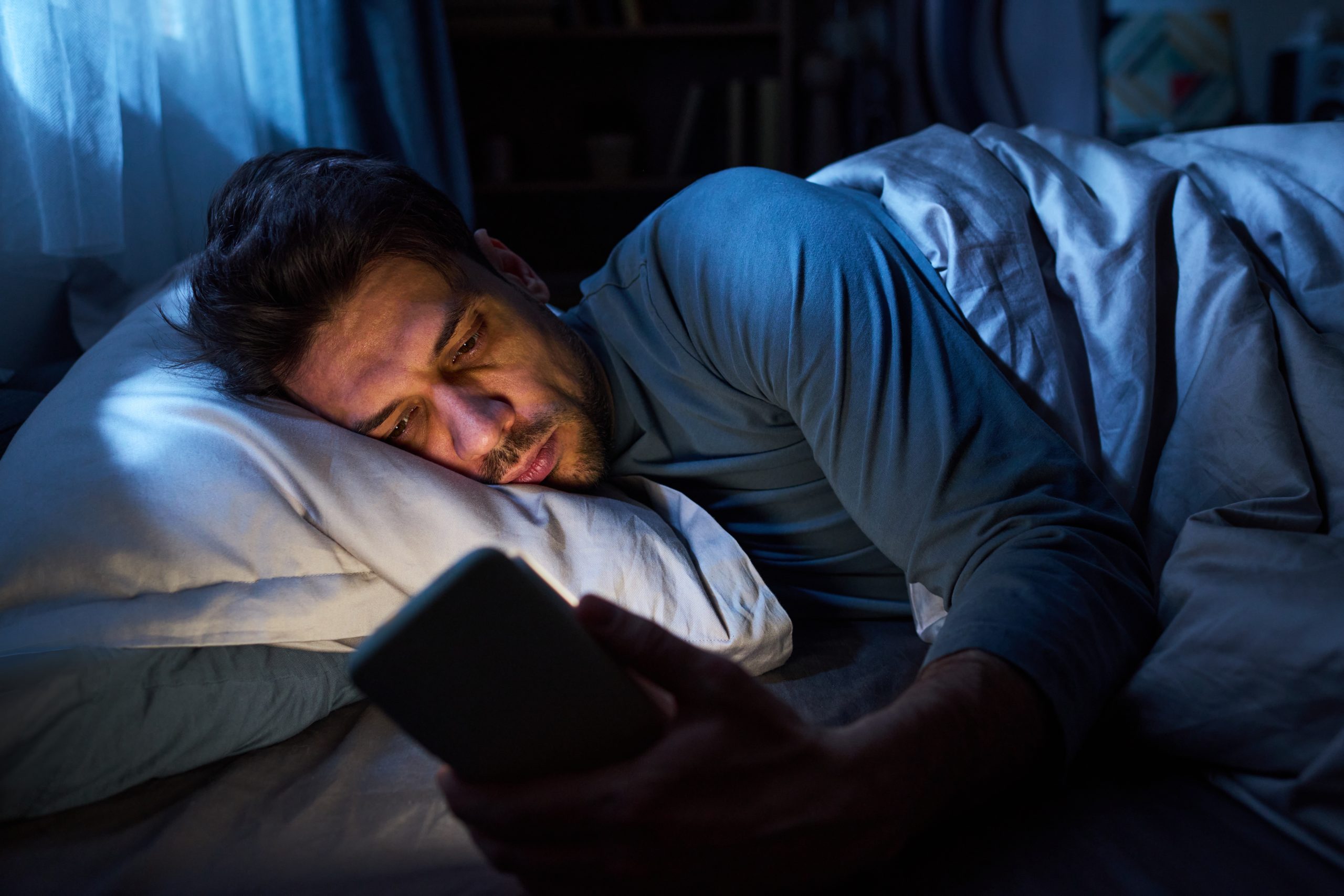Queer person looking at their phone with a tense expression, representing the emotional impact of online hate speech during Pride Month