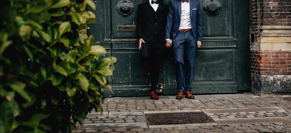 Same-sex couple holding hands outside a historic building, representing connection, commitment, and LGBTQ+ relationships.