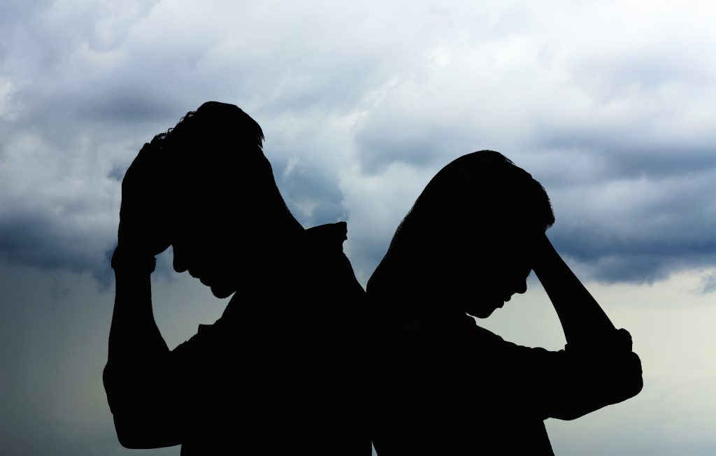 Couple sitting back-to-back outdoors beneath a cloudy sky
