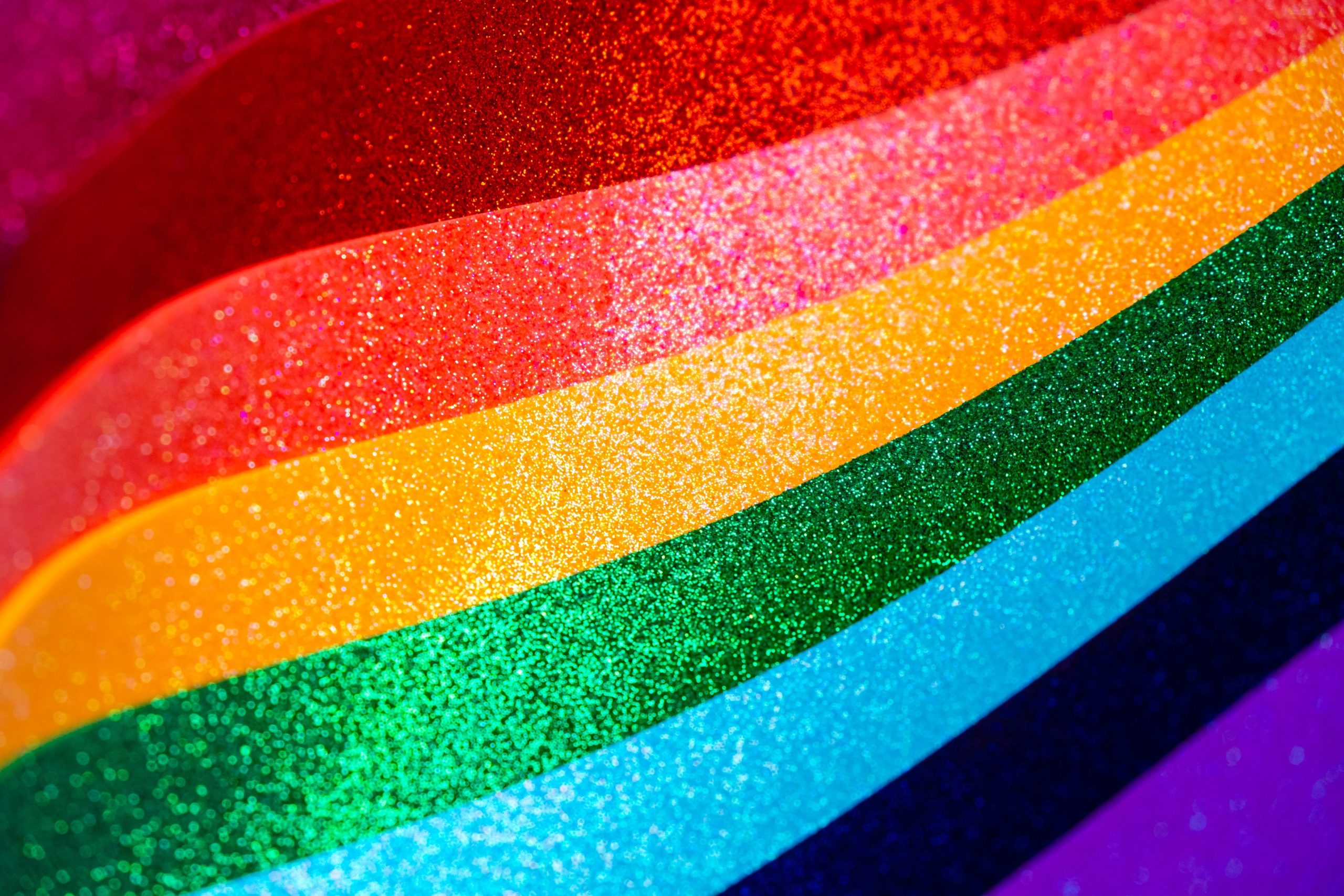 Close-up of a glittering rainbow Pride flag with vibrant red, orange, yellow, green, blue, and purple stripes shimmering in the light.