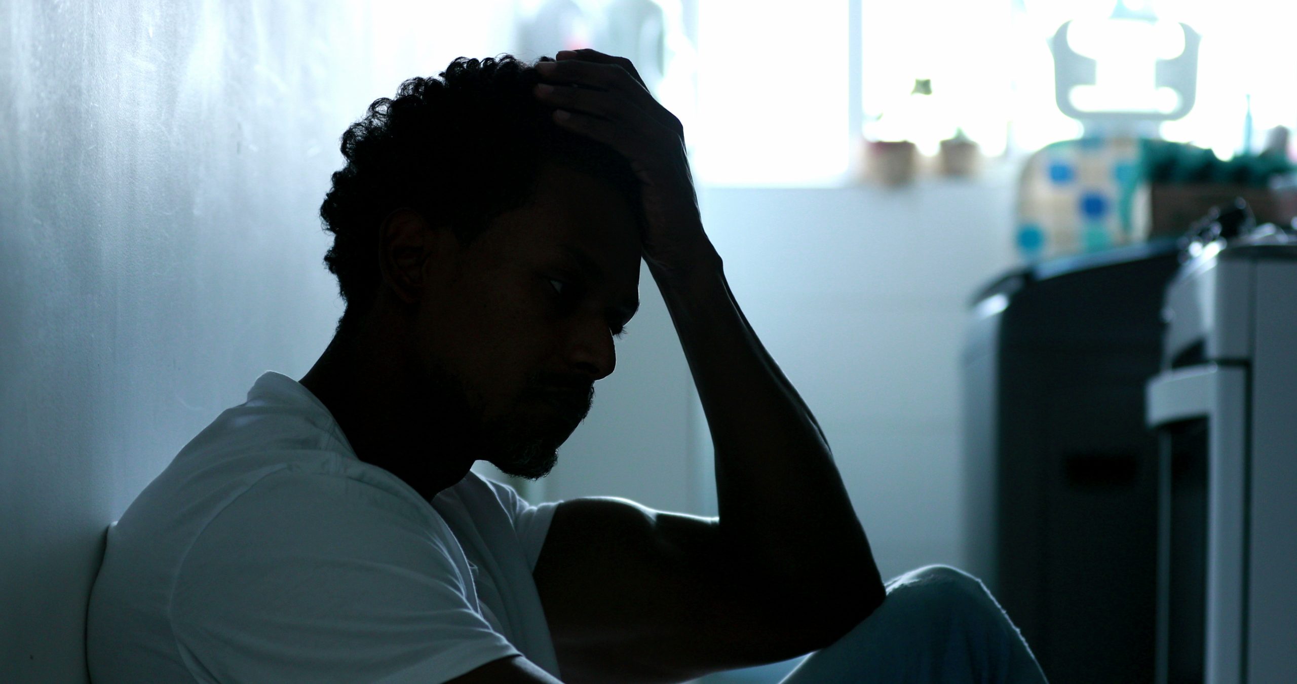 Person sitting on the floor with their head in their hand, appearing overwhelmed by anxiety, chronic stress, or emotional exhaustion.