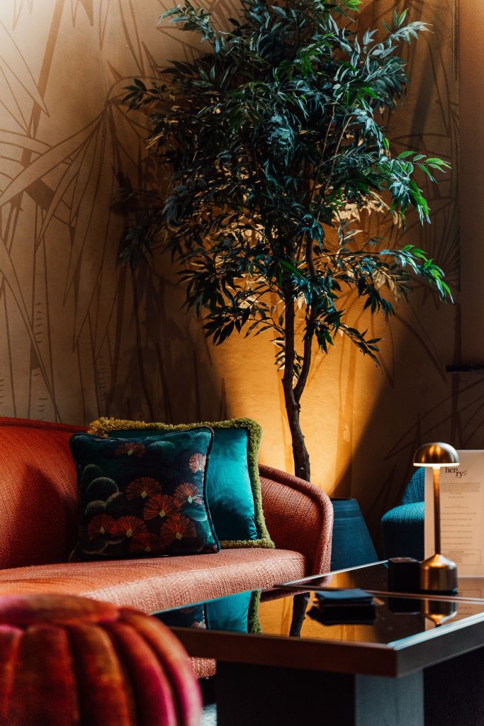 Warm, inviting therapy office with a curved blush sofa, colorful accent pillows, indoor plants, and soft ambient lighting creating a comfortable counseling environment.