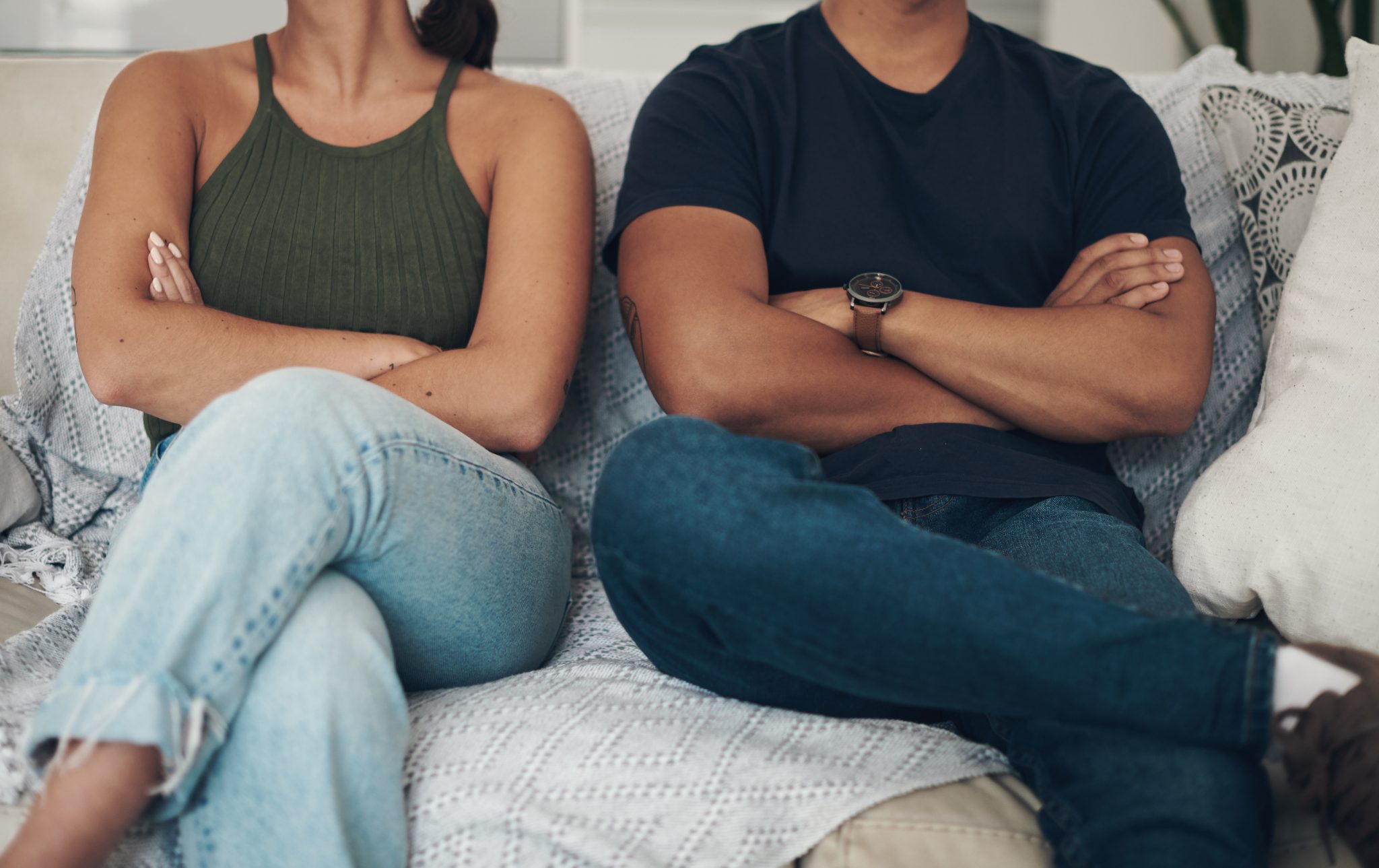 Couple sitting on a couch with crossed arms and closed body language, illustrating emotional distance, unresolved conflict, and relationship disconnection.