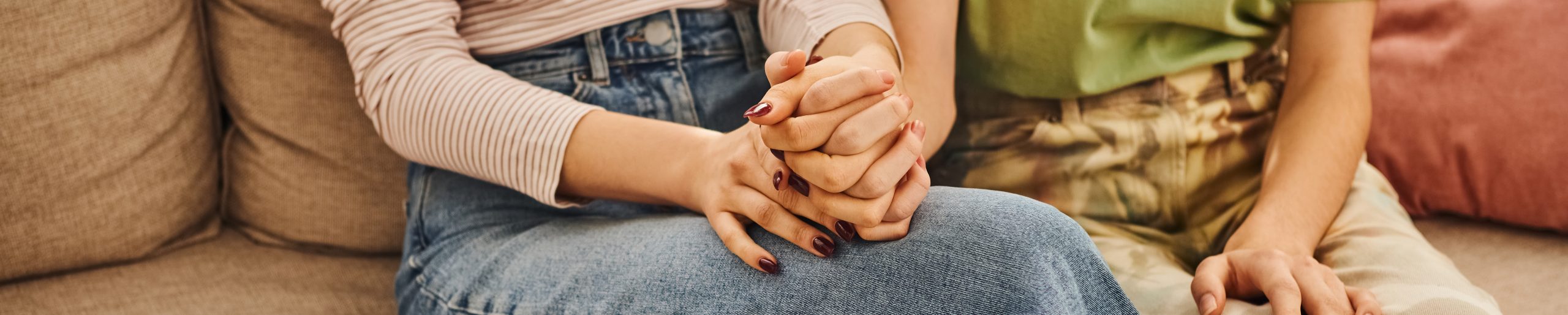 LGBTQ+ couple sitting together and holding hands, representing connection, support, and the unique experiences that shape queer relationships.