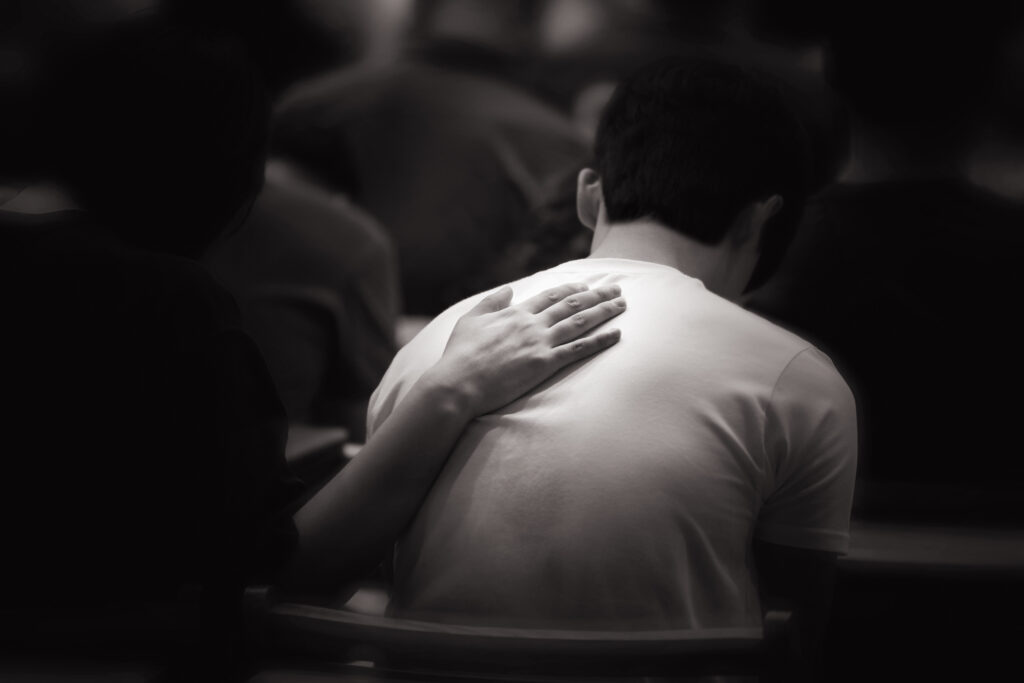 Man sitting in a church pew with a hand resting on his back