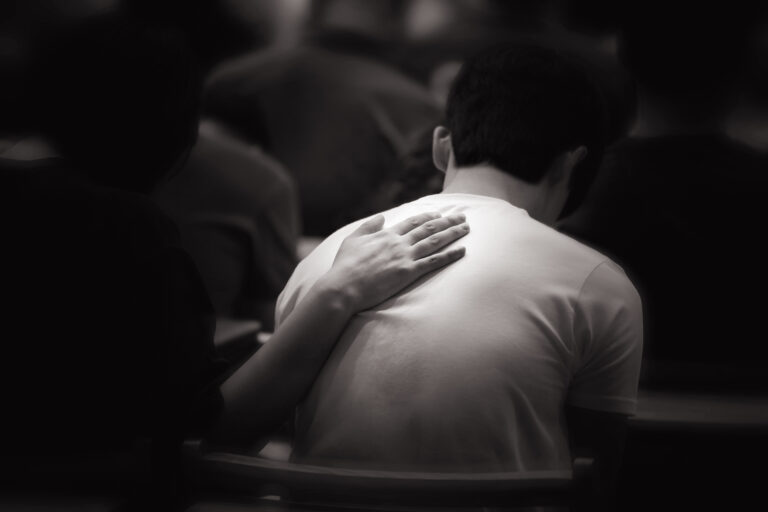 Man sitting in a church pew with a hand resting on his back