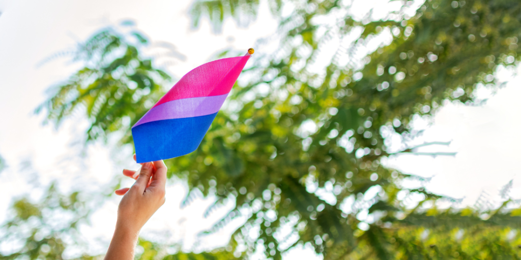 Hand holding a bisexual pride flag outdoors, representing bisexual identity, visibility, and belonging.